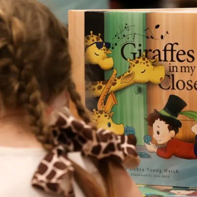 Little girl with Giraffes in my closet book in the background