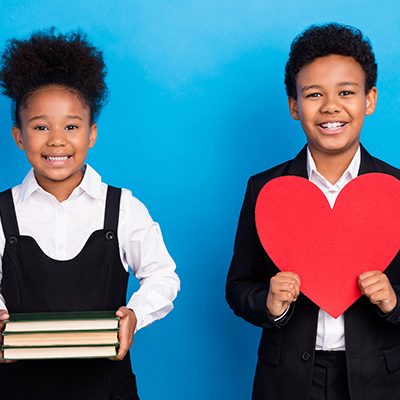 Photo of dark skin little small people friends hold hands books heart red paper wear uniform isolated on blue color background Children holding books and hearts
